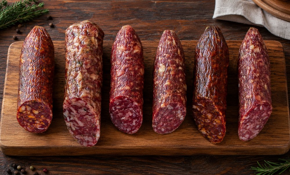 Assorted dry-cured hog casing salami sliced on wooden board